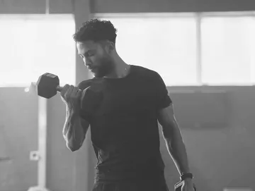 Man performing a dumbbell curl in a gym, shown in black and white